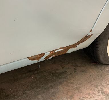 A white car with rust on the side of it is parked in a garage.