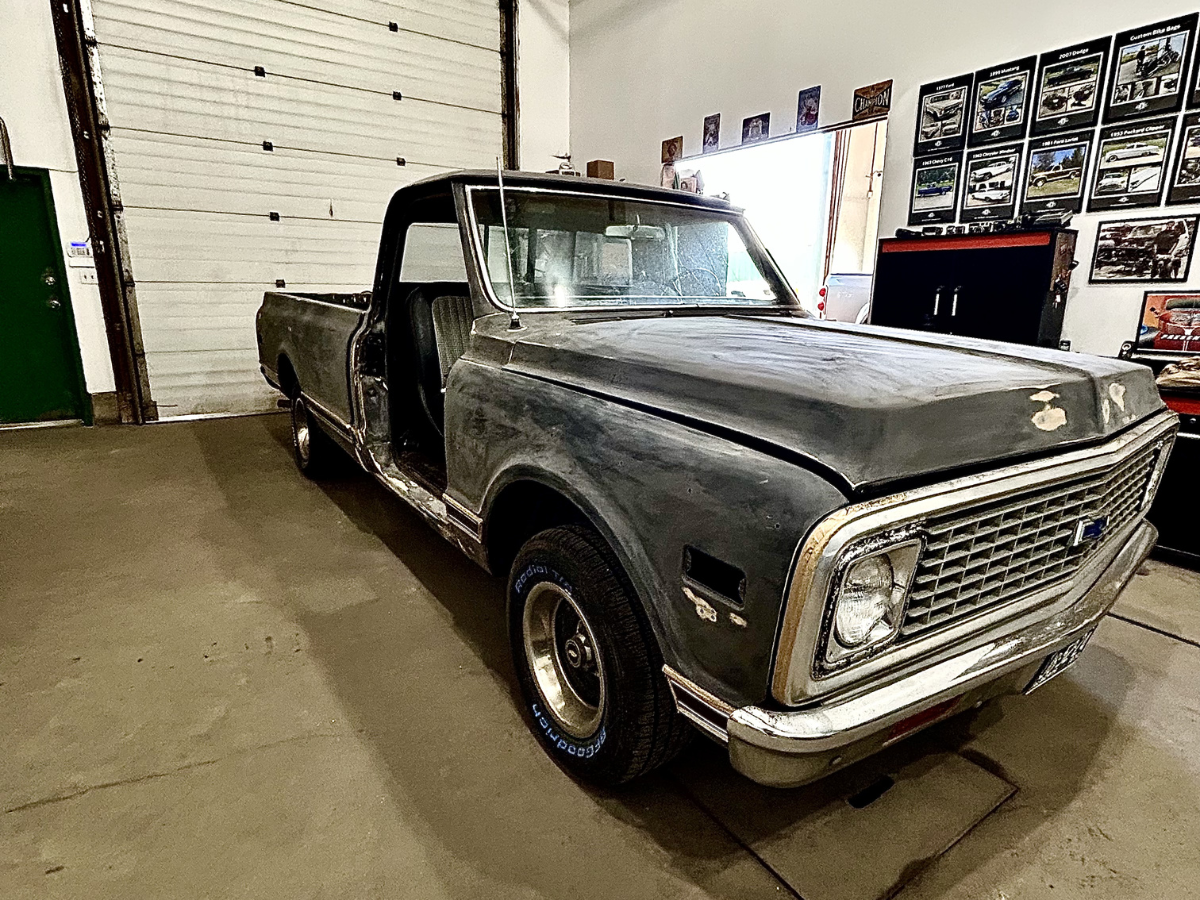 Vintage black pickup truck parked indoors in a garage, viewed from the front-left side.