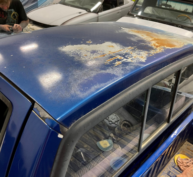 The roof of a blue car is covered in rust