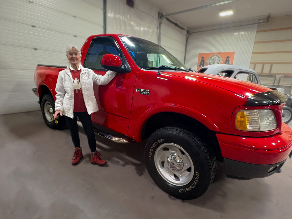 Woman standing beside a red pickup truck in a garage showroom
