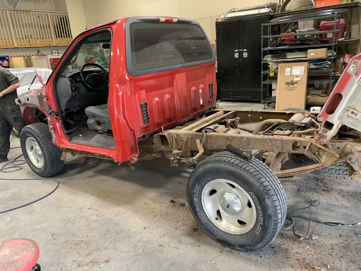 Red pickup truck with cab removed, exposed chassis, in a workshop garage.