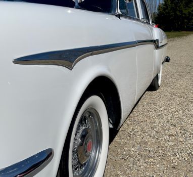 A white car with white tires is parked on a gravel road