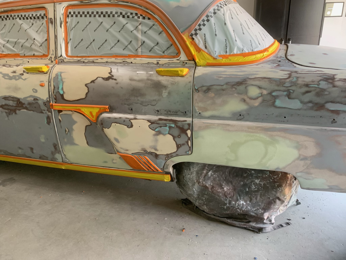Rusty vintage car body with patched panels and orange trim in a garage