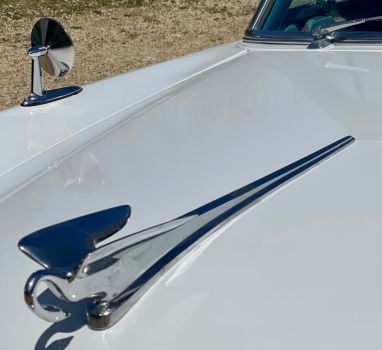 A white car with a chrome hood ornament on it