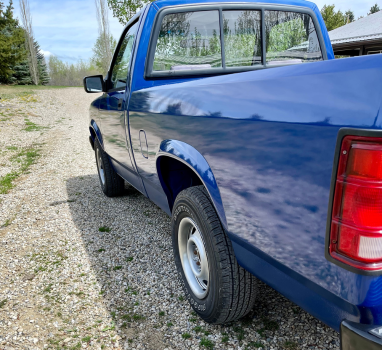 A blue truck is parked on a gravel road