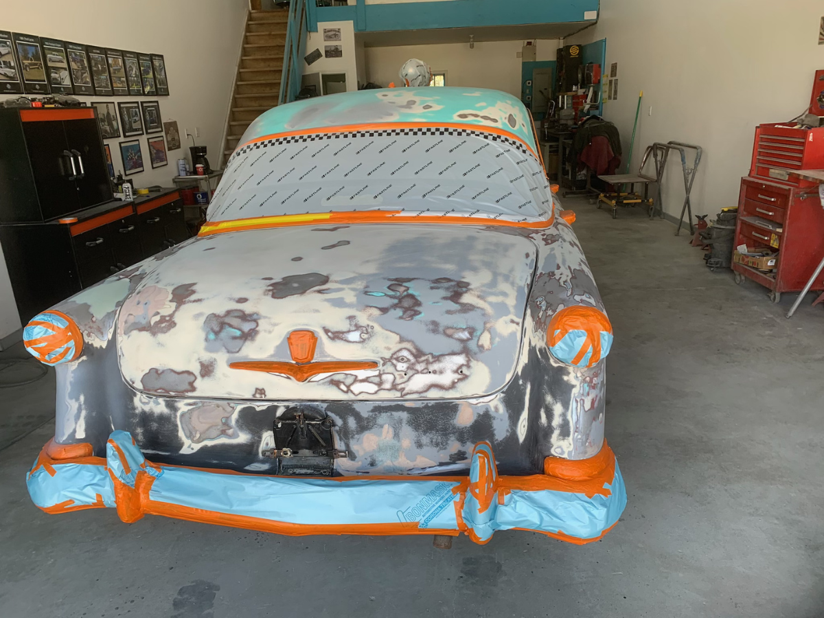 Painted car with orange tape in a garage, front view, surrounded by tools and clutter.