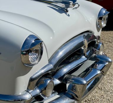 A white car with chrome trim is parked on gravel