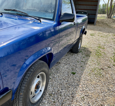 A blue truck is parked in a gravel area