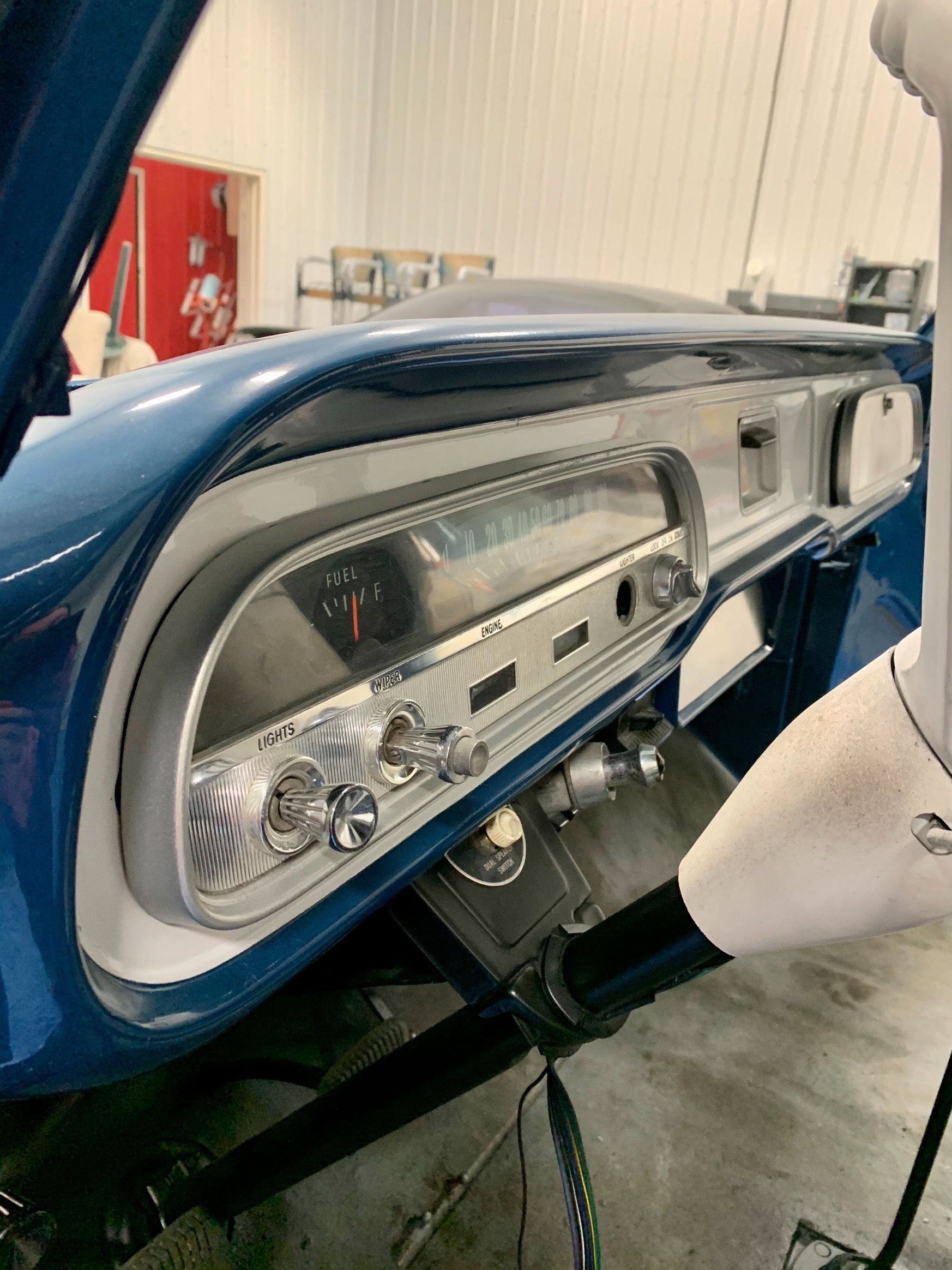 The dashboard of a blue car with the hood up in a garage.