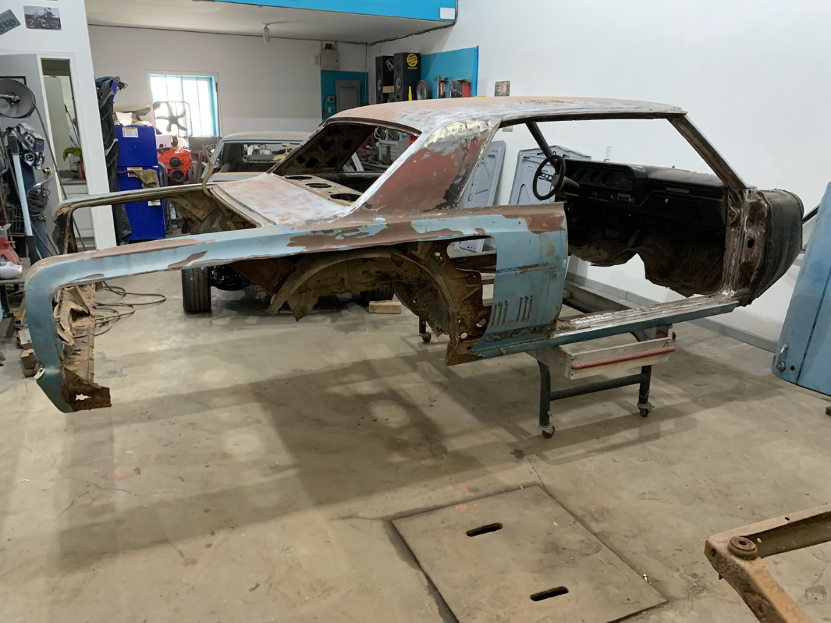 Rusty stripped car body on a stand in a workshop, with missing doors and interior.