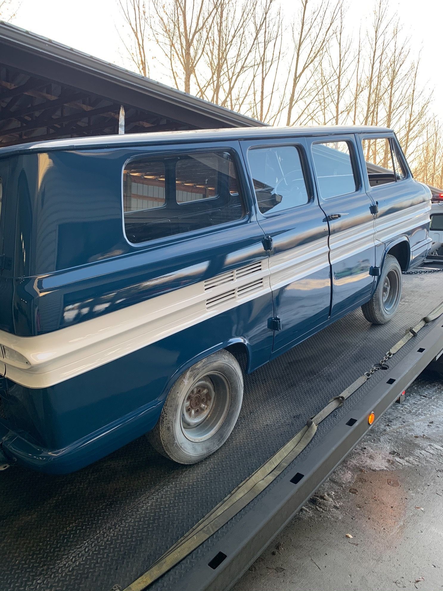 A blue van is sitting on top of a tow truck.