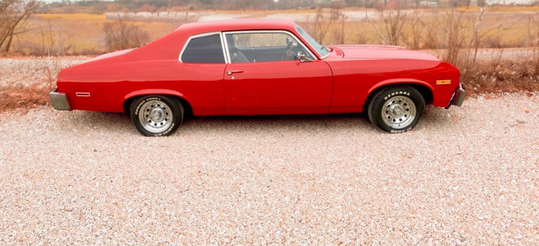 A red car is parked in a gravel lot.