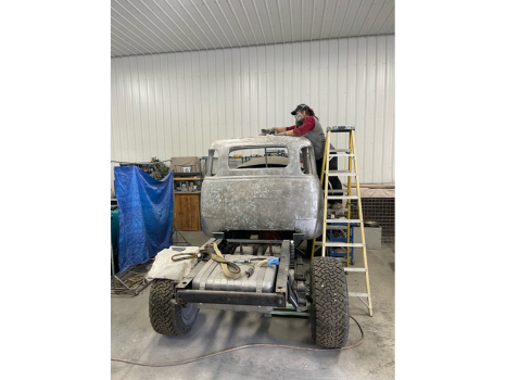 A man is sitting on a ladder working on a truck in a garage.