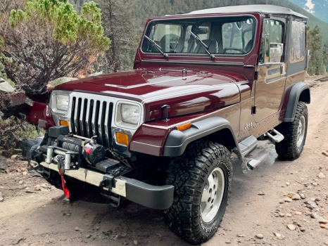 A red jeep is parked on a dirt road.