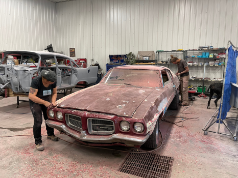 A man is working on a rusty car in a garage.