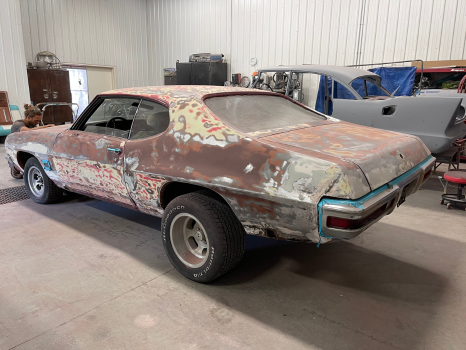An old rusty car is sitting in a garage.