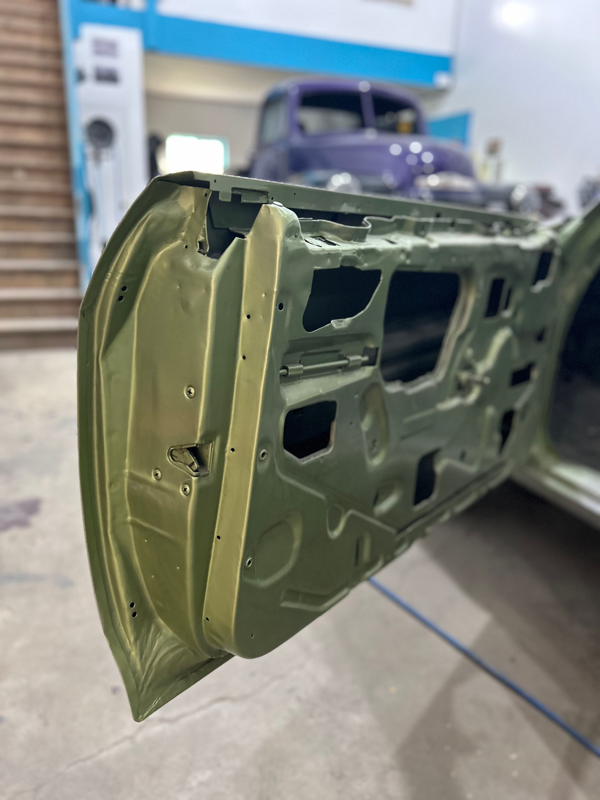 A close up of a car door with a purple truck in the background.