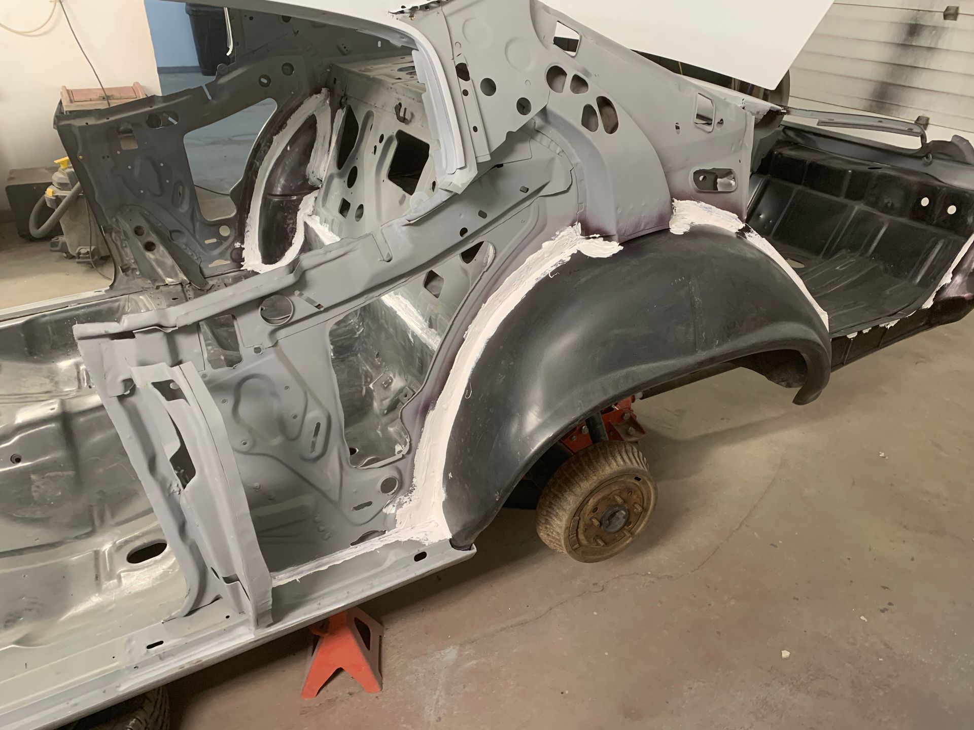 A skeleton of a car is sitting on a jack in a garage.