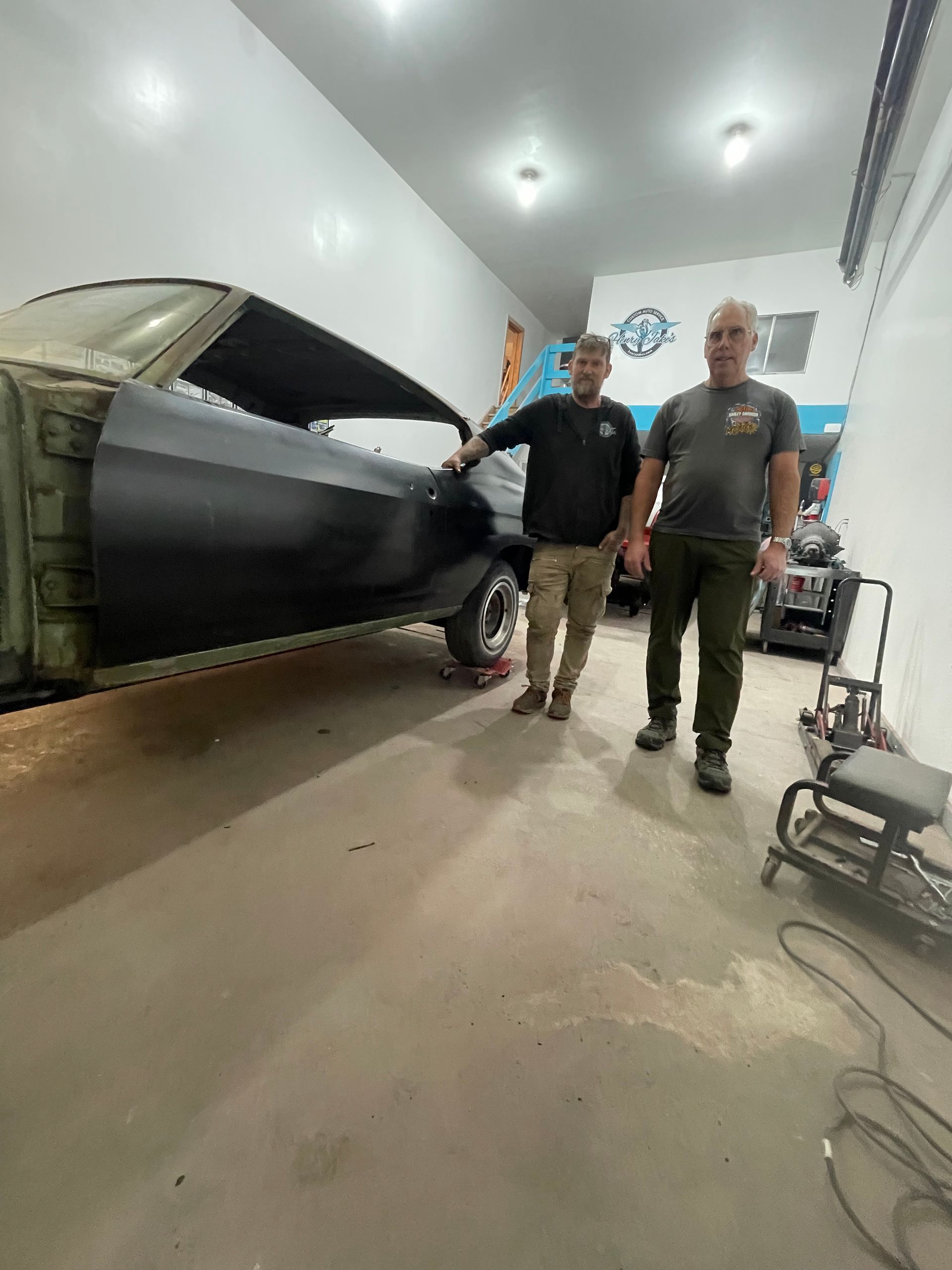 Two men are standing next to a car in a garage.