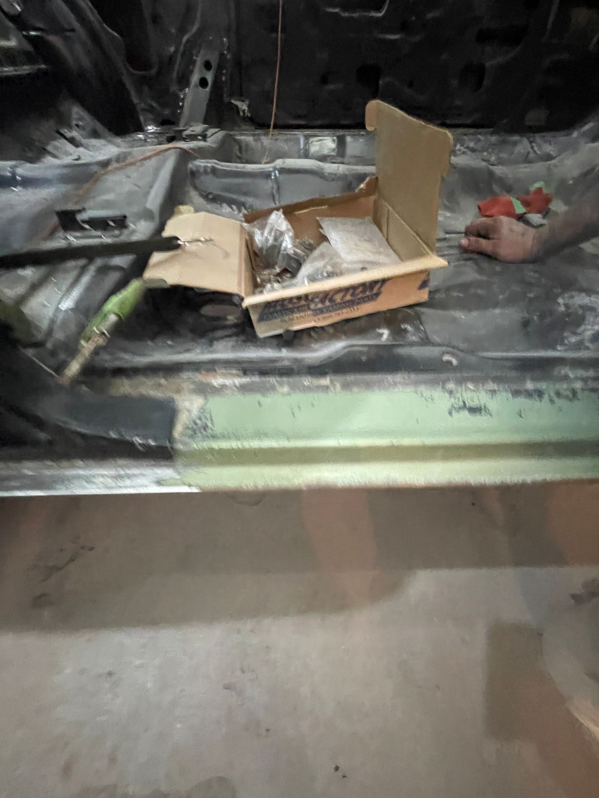 A person is working on a car with a box of tools on the floor.