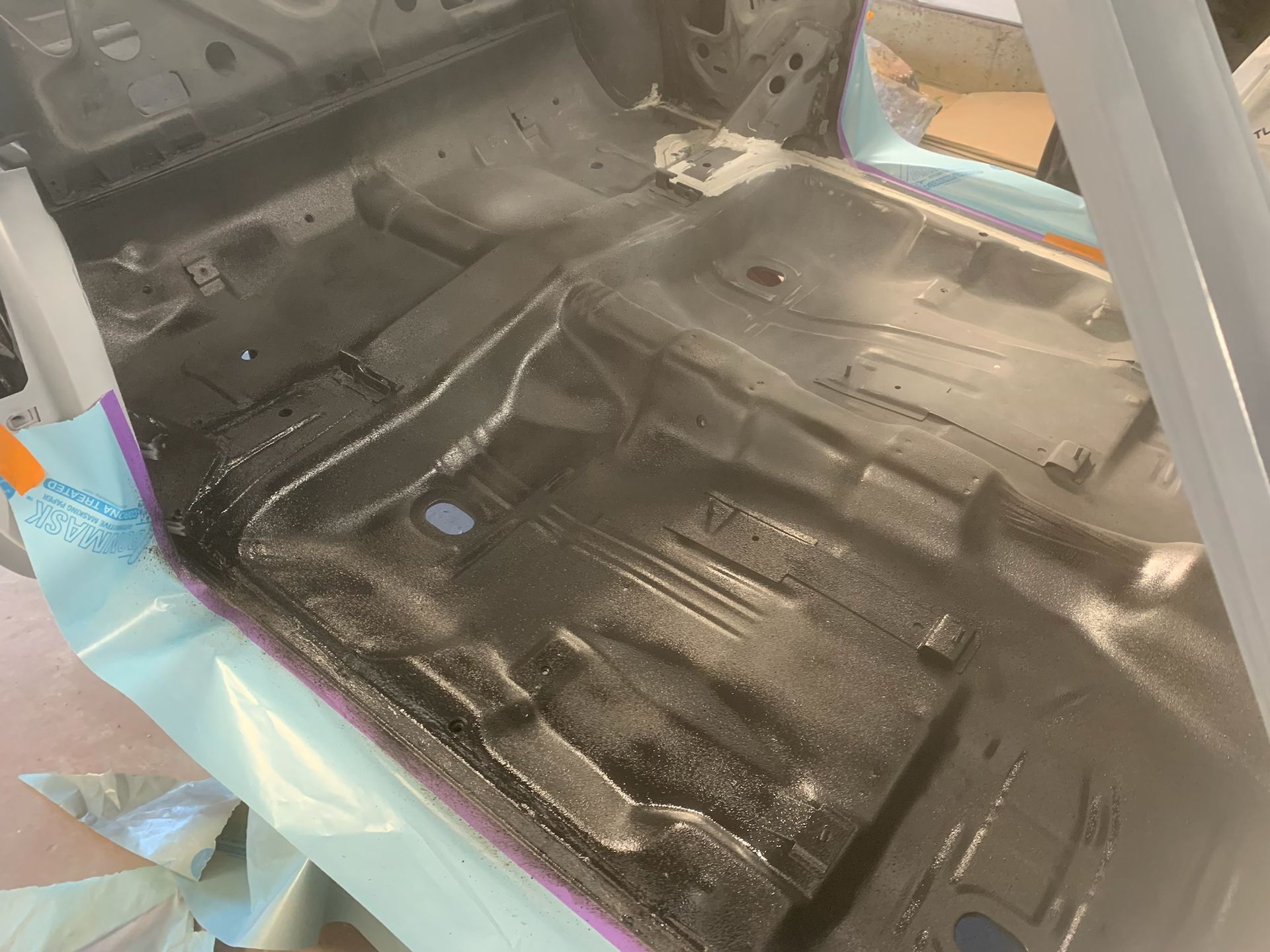 The bottom of a car is being painted black.