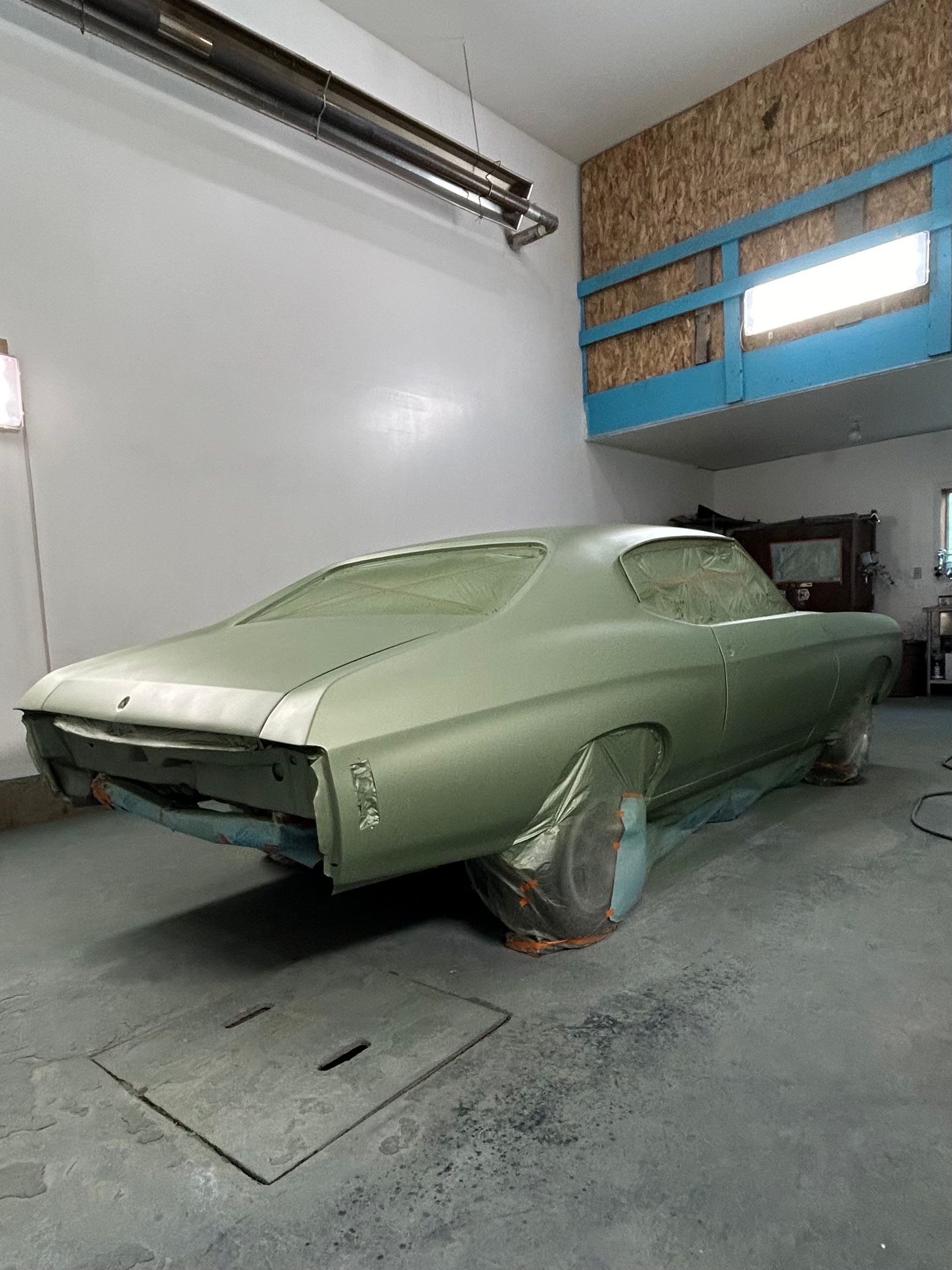 A green car is sitting in a garage being painted.