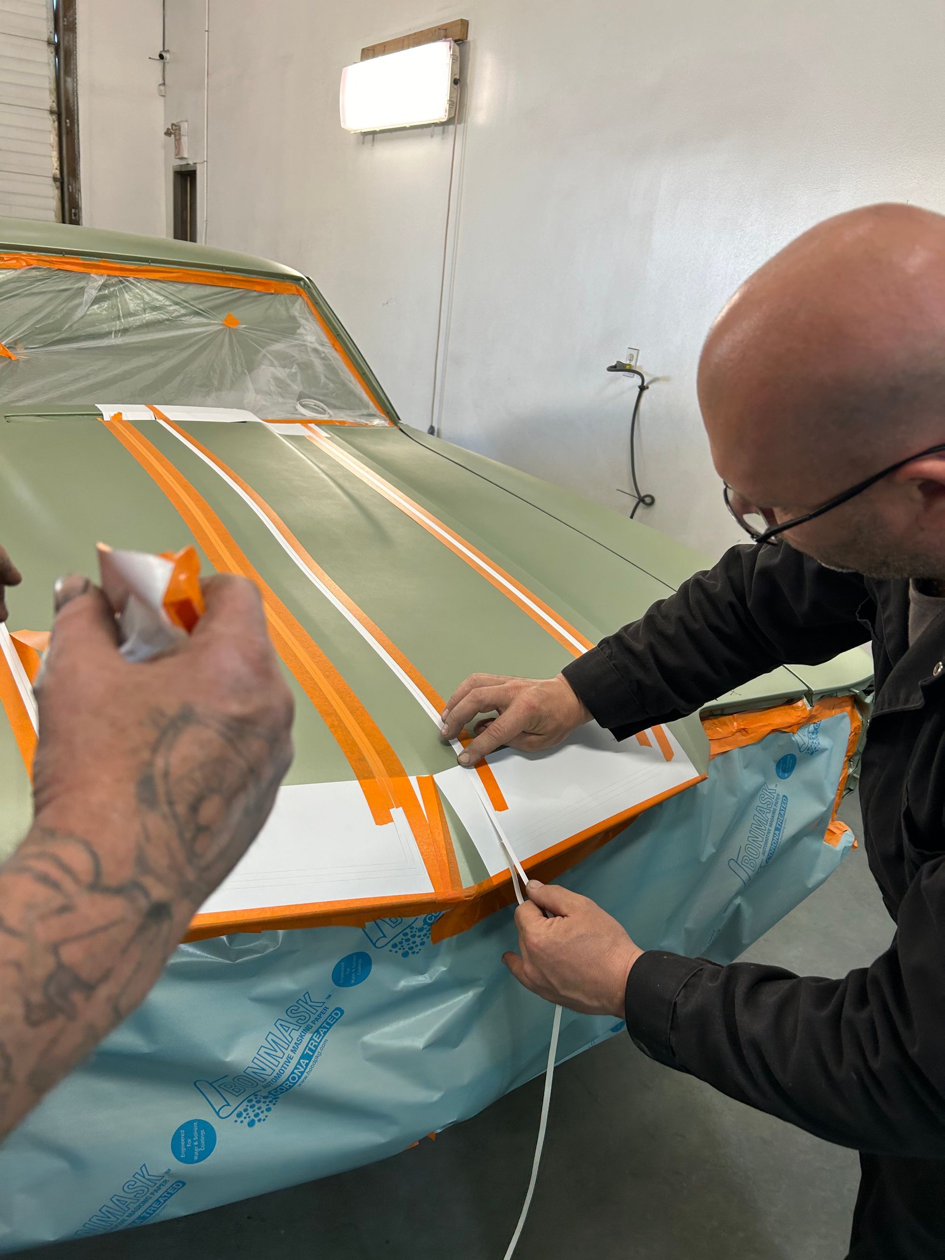A man is painting a car with orange and white stripes