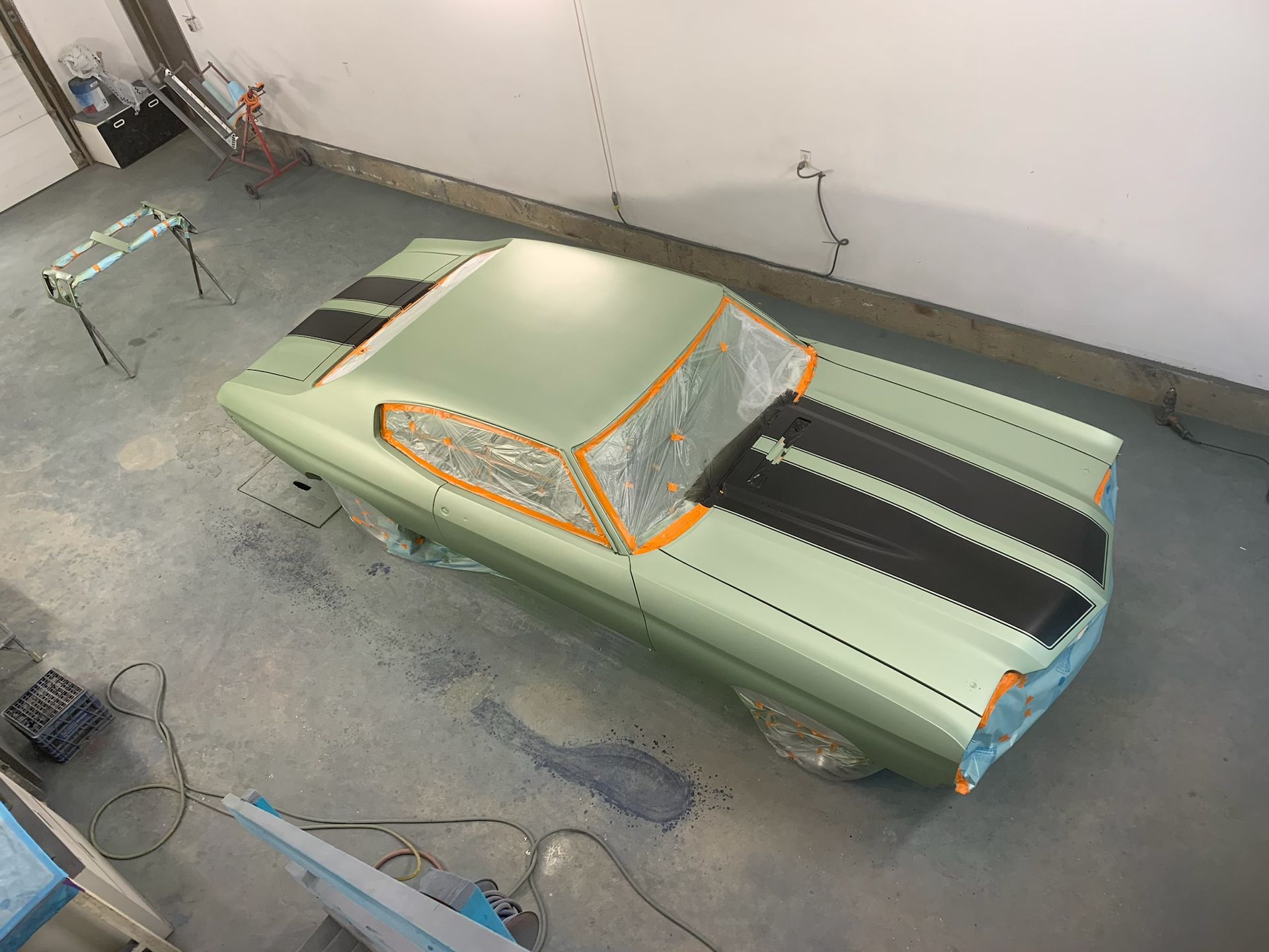 A green car with black stripes is sitting in a garage.