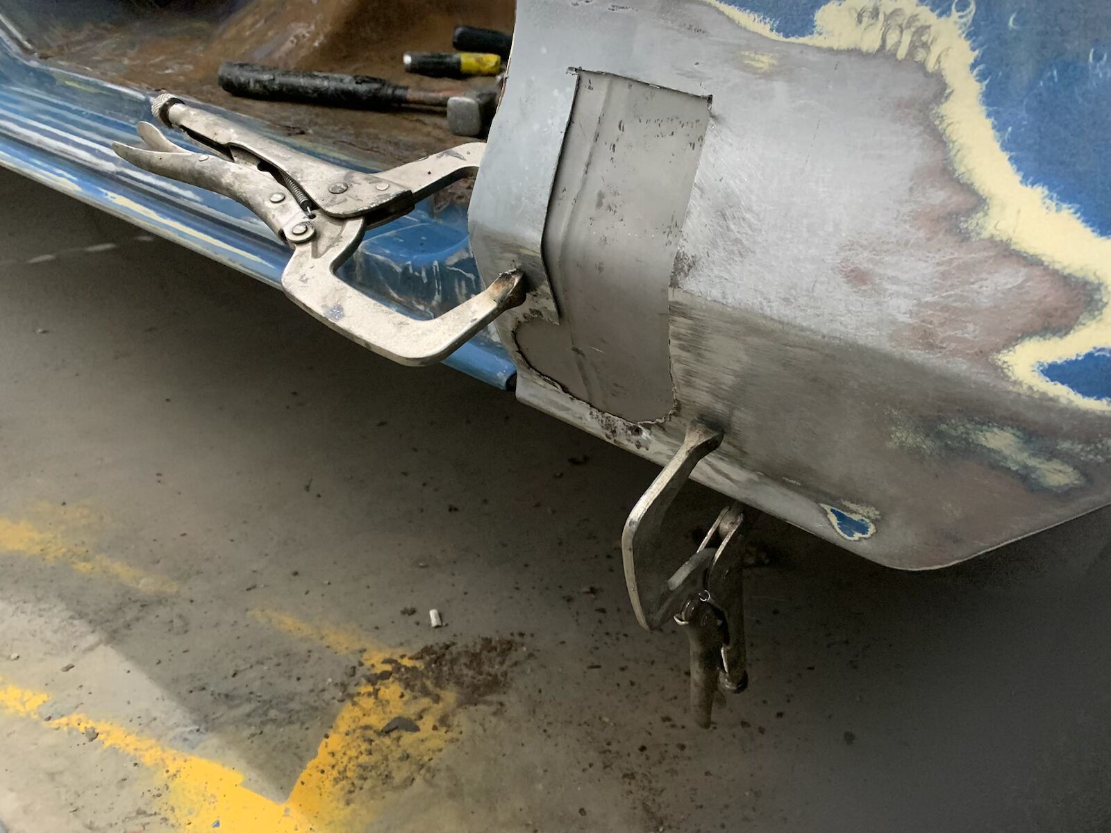 Close-up of a damaged gray car’s rear bumper and tow hitch on a concrete surface, with paint scratches visible