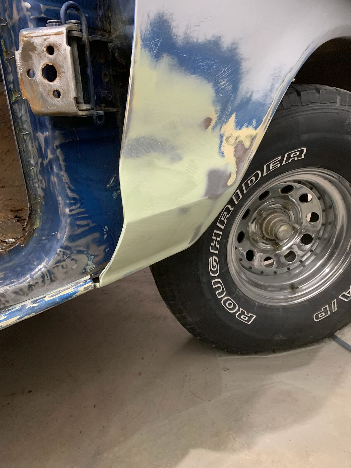 Partially repaired car body with primer and body filler near rear wheel and tire