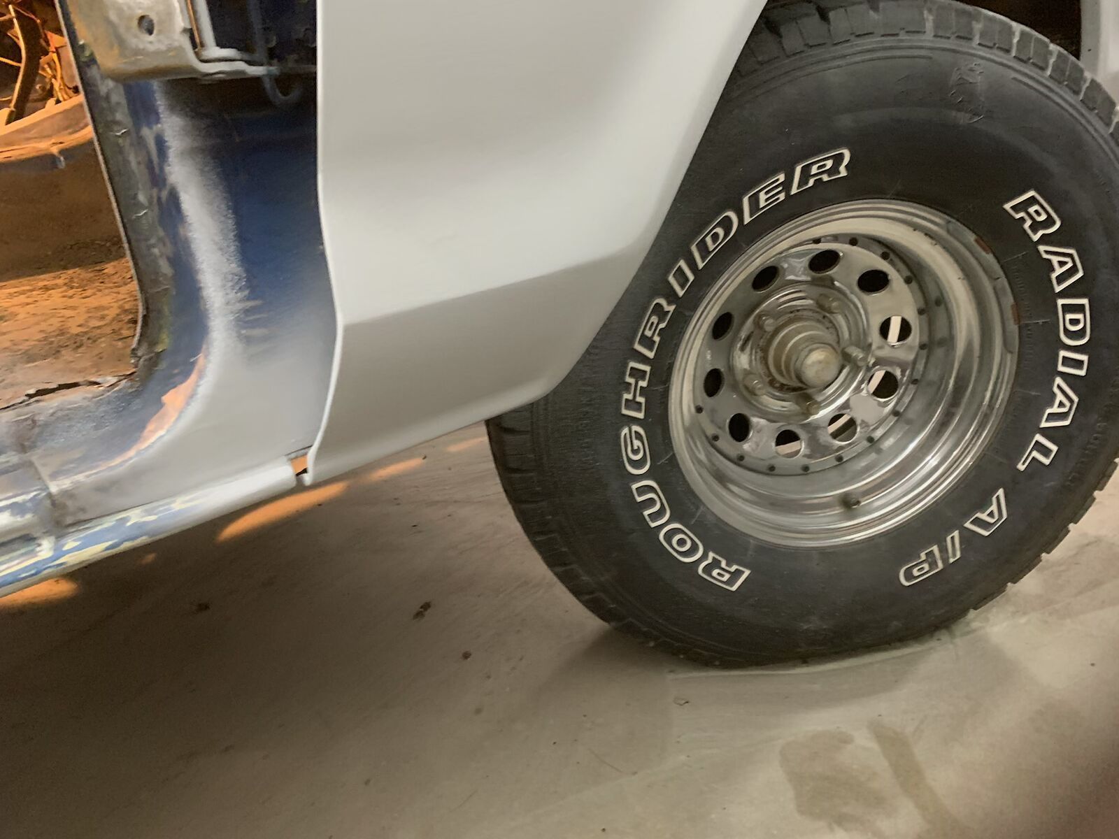 Close-up of a car’s front wheel and rusted blue body panel in a garage.