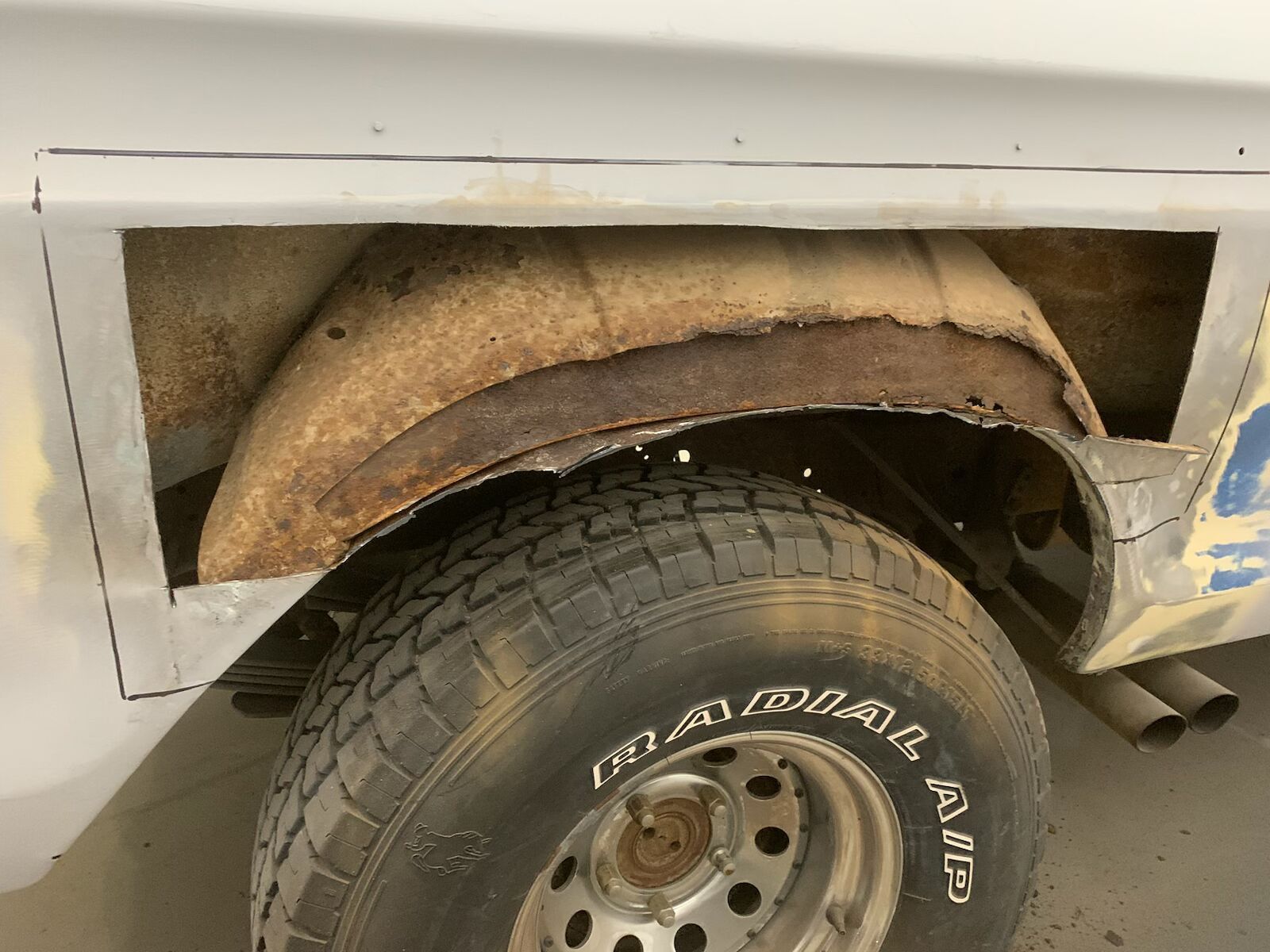 Rusty truck wheel well with damaged fender above a tire, showing corrosion and wear