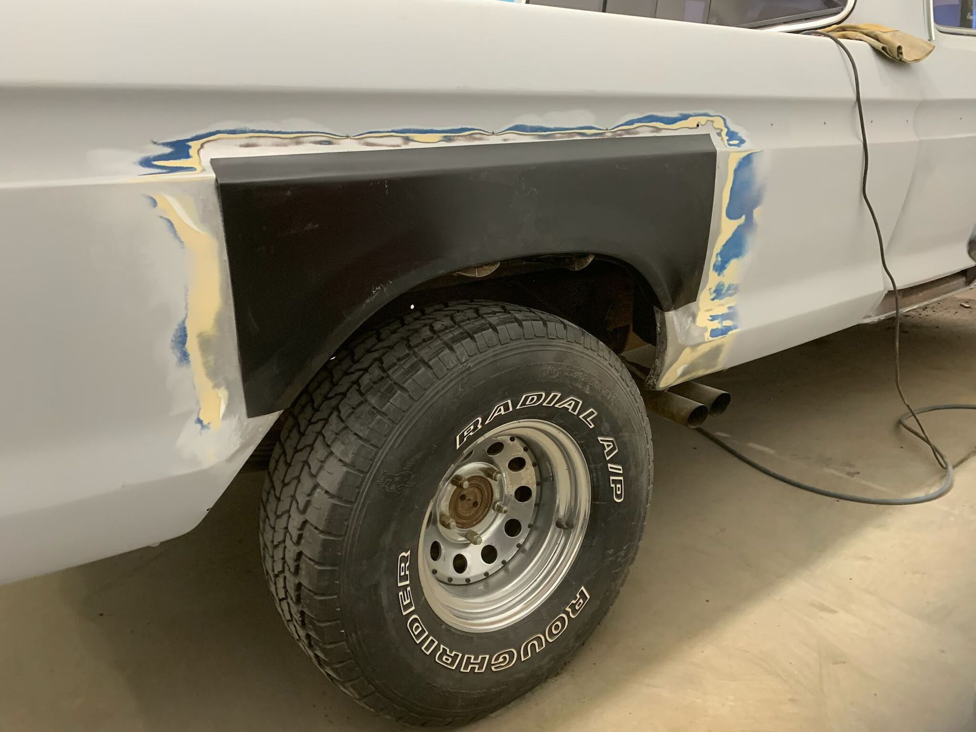 Car with primered rear wheel arch and tape masking for bodywork repair, wheel installed in a garage