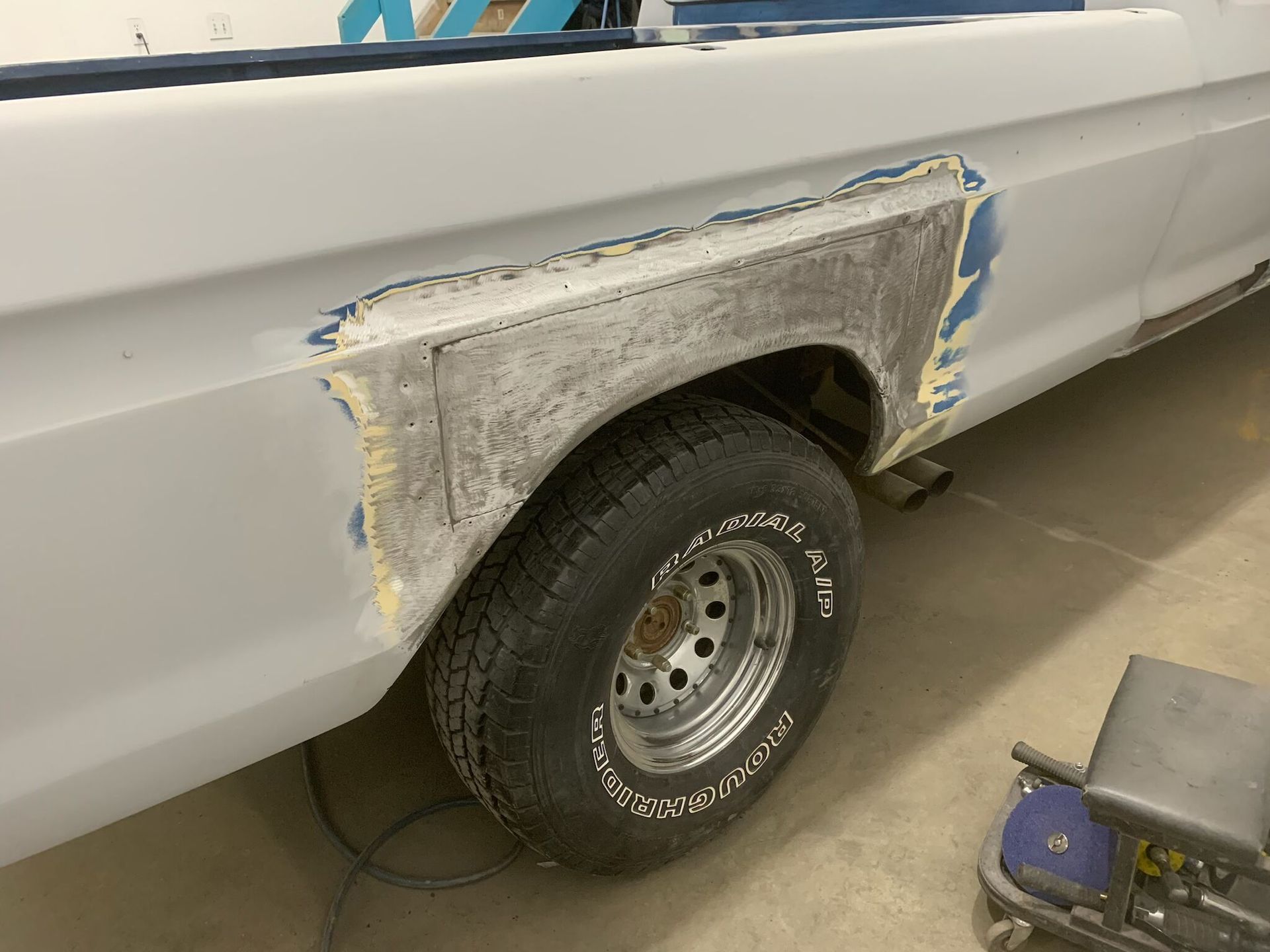 White truck with a repaired, sanded rear wheel arch and a visible tire in a workshop.