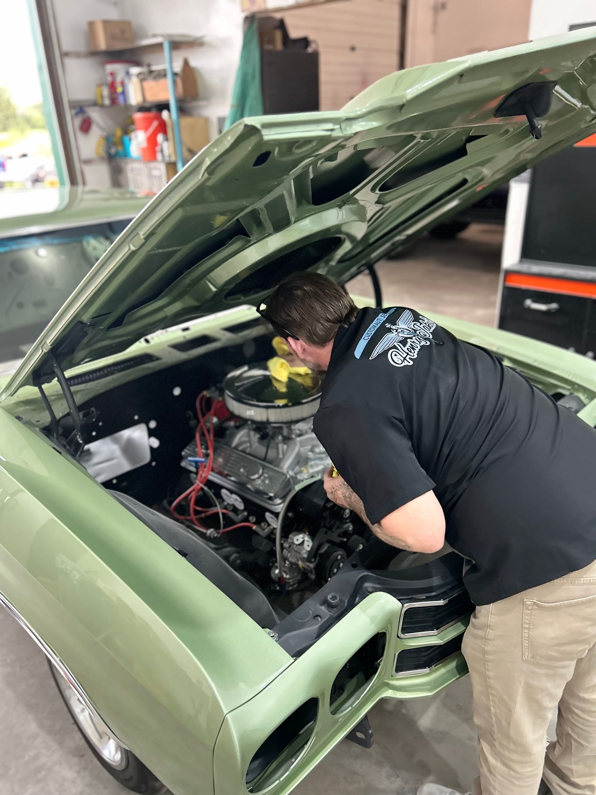 A man is working on the engine of a green car.