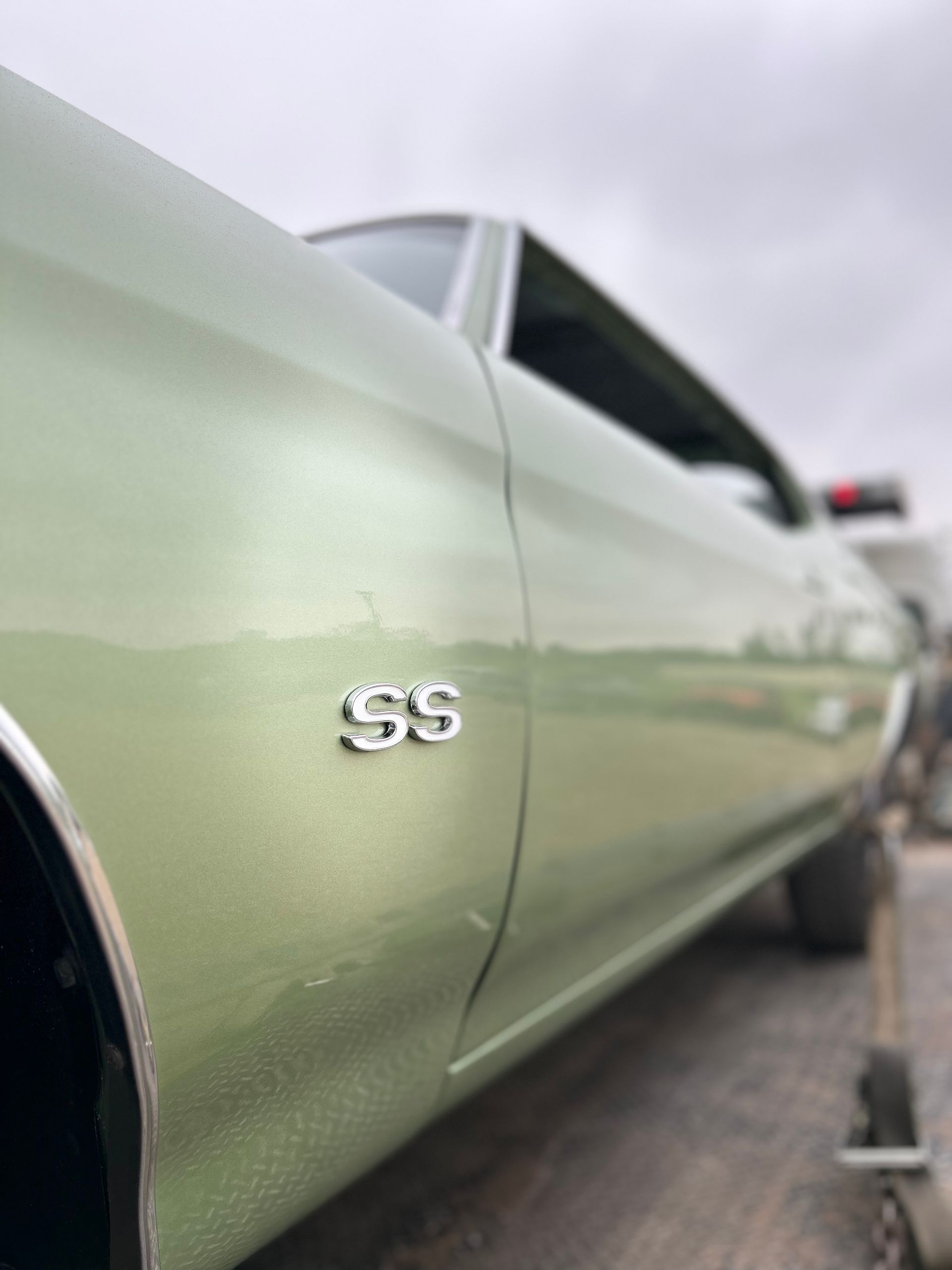 Close-up of a silver classic car with an SS badge on the side panel outdoors