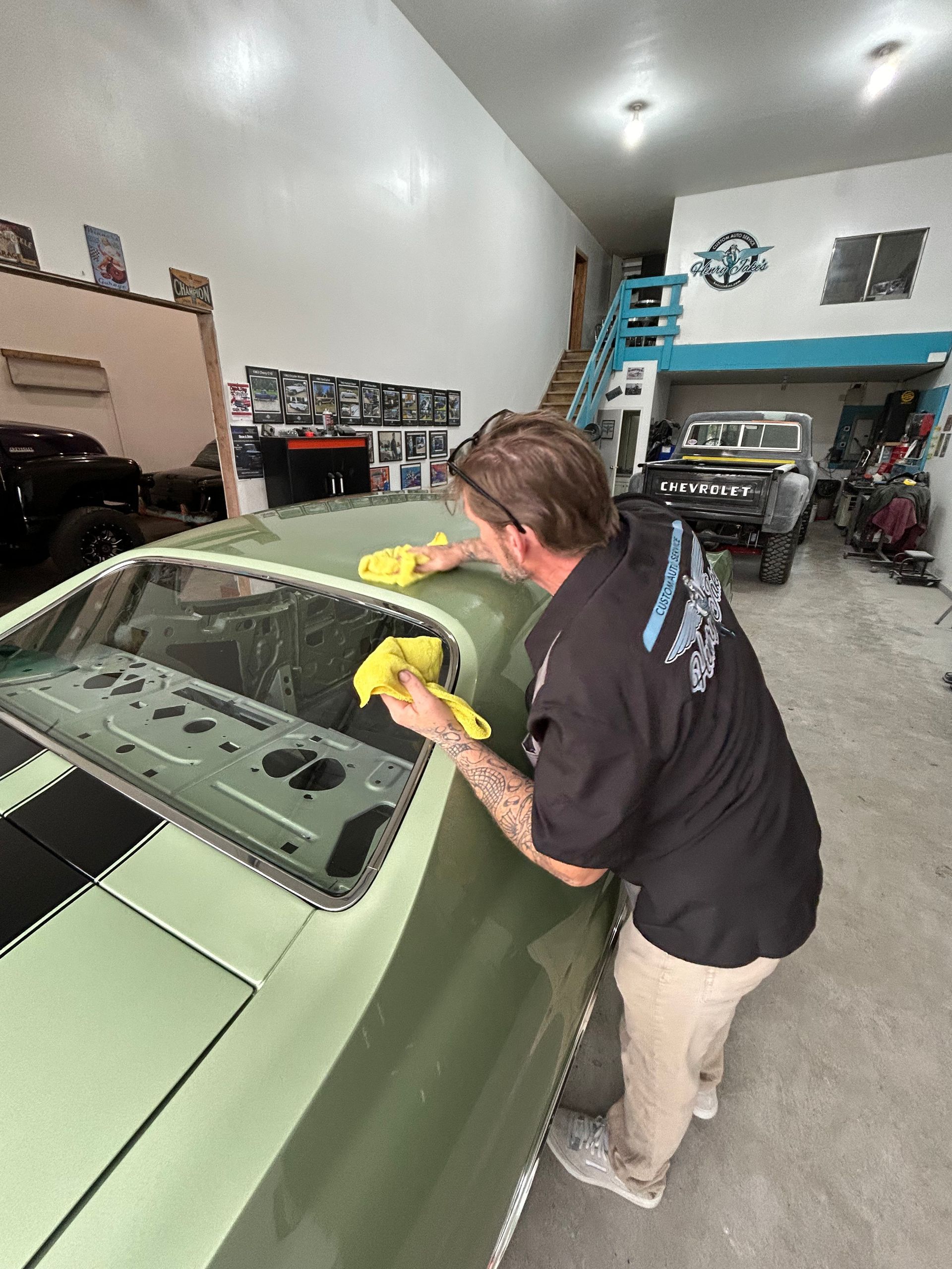 A man is cleaning the windshield of a green car in a garage.