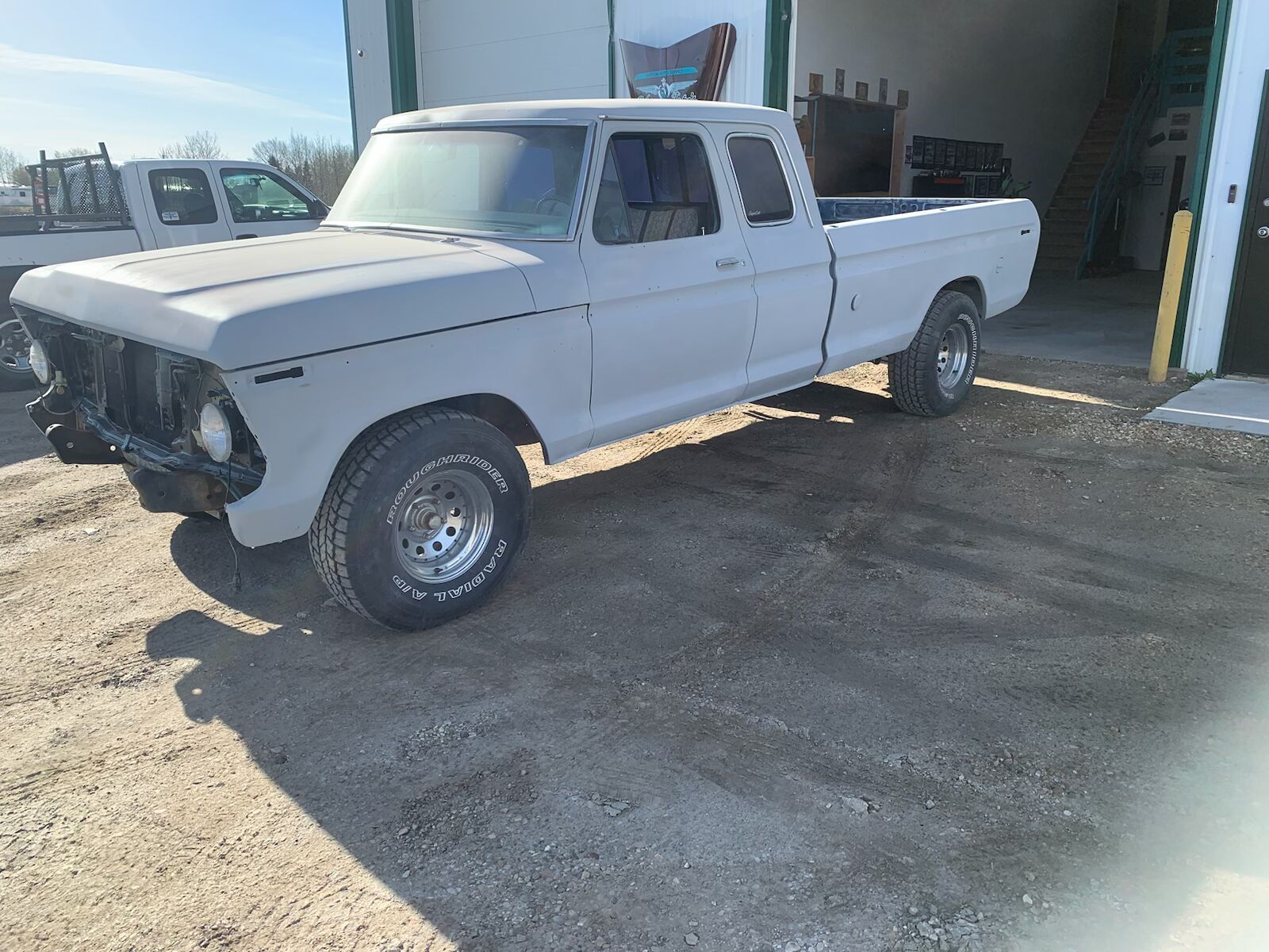White vintage pickup truck parked outside a garage on a wet concrete lot