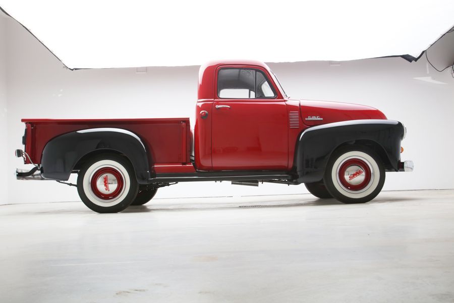 A red truck with white tires is parked in front of a white wall.