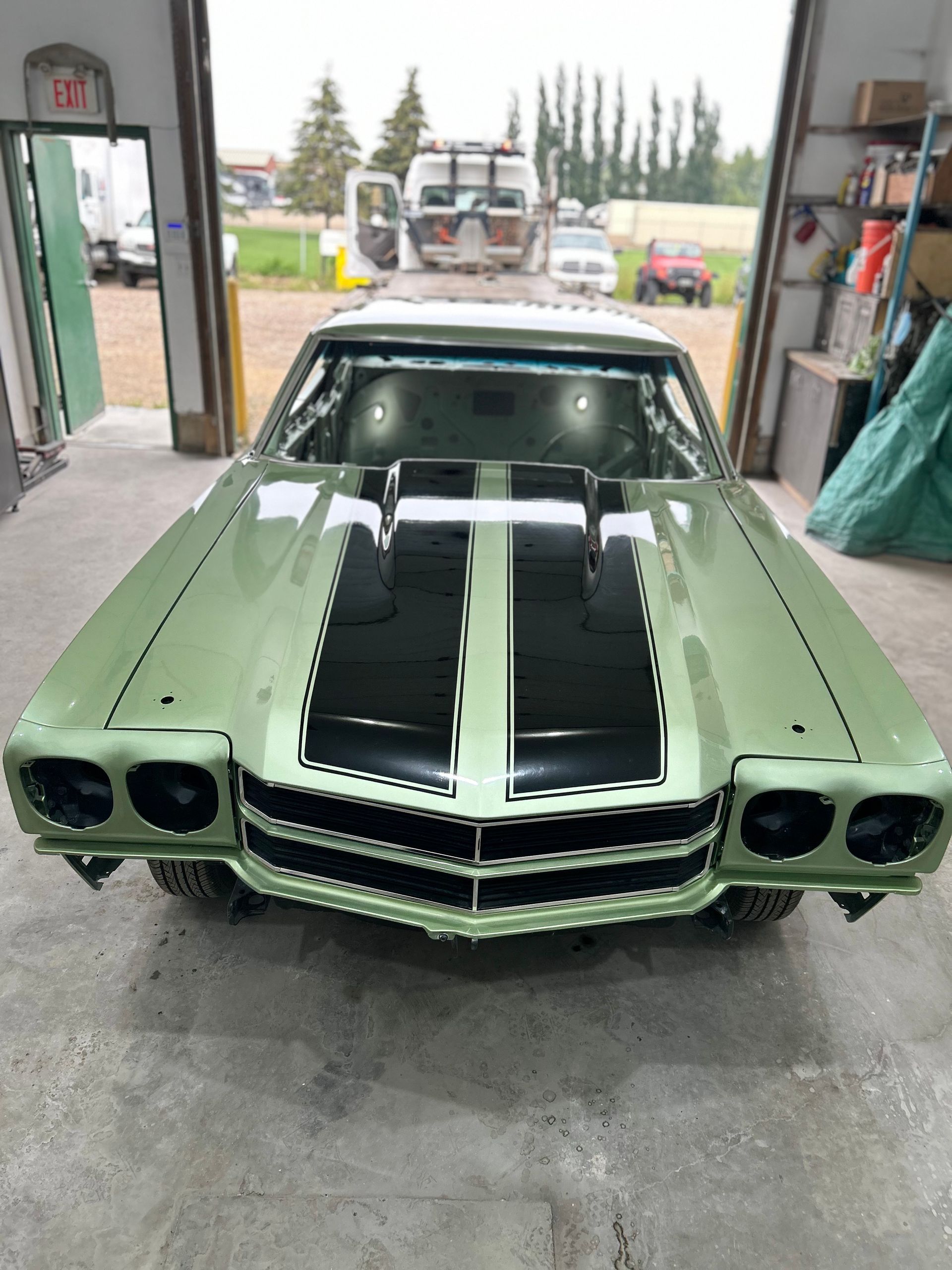 A green car with black stripes is parked in a garage.