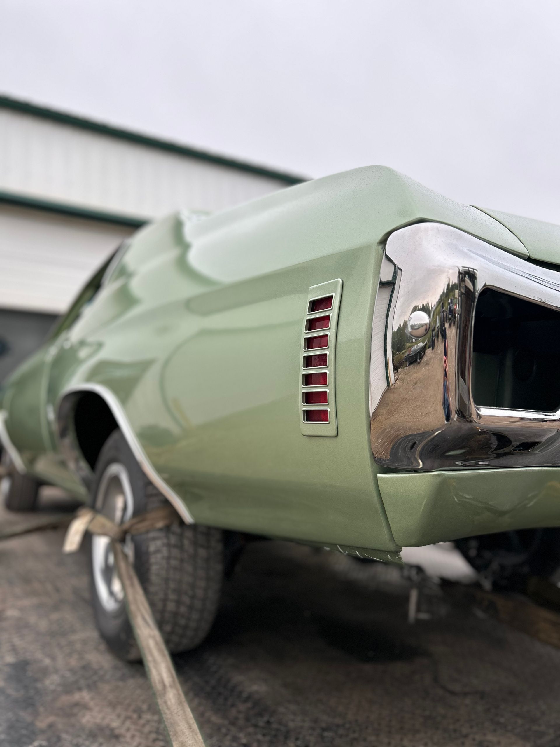 A green car with a chrome bumper is parked in front of a garage.