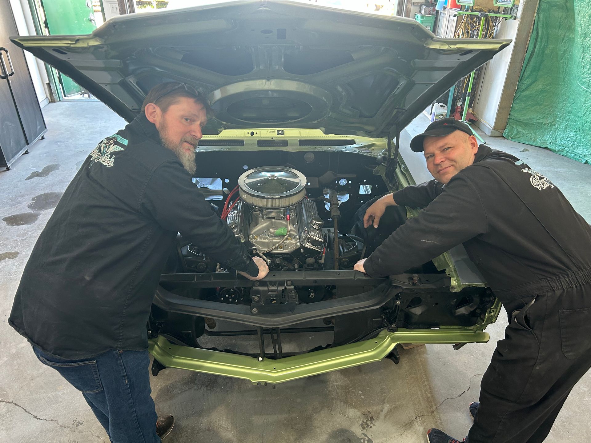 Two men are working on the engine of a green car.