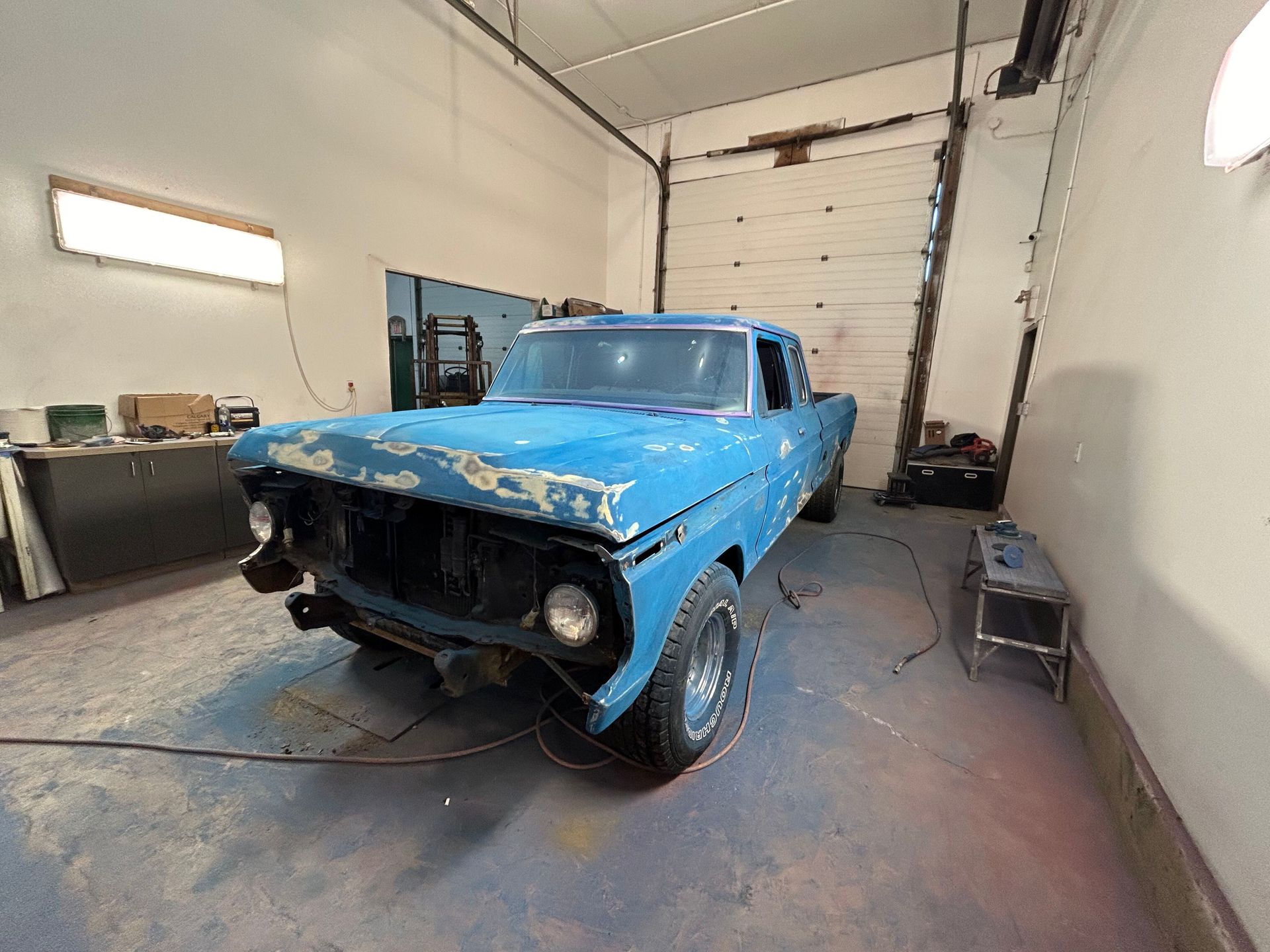 Blue classic car with a missing front bumper in a garage