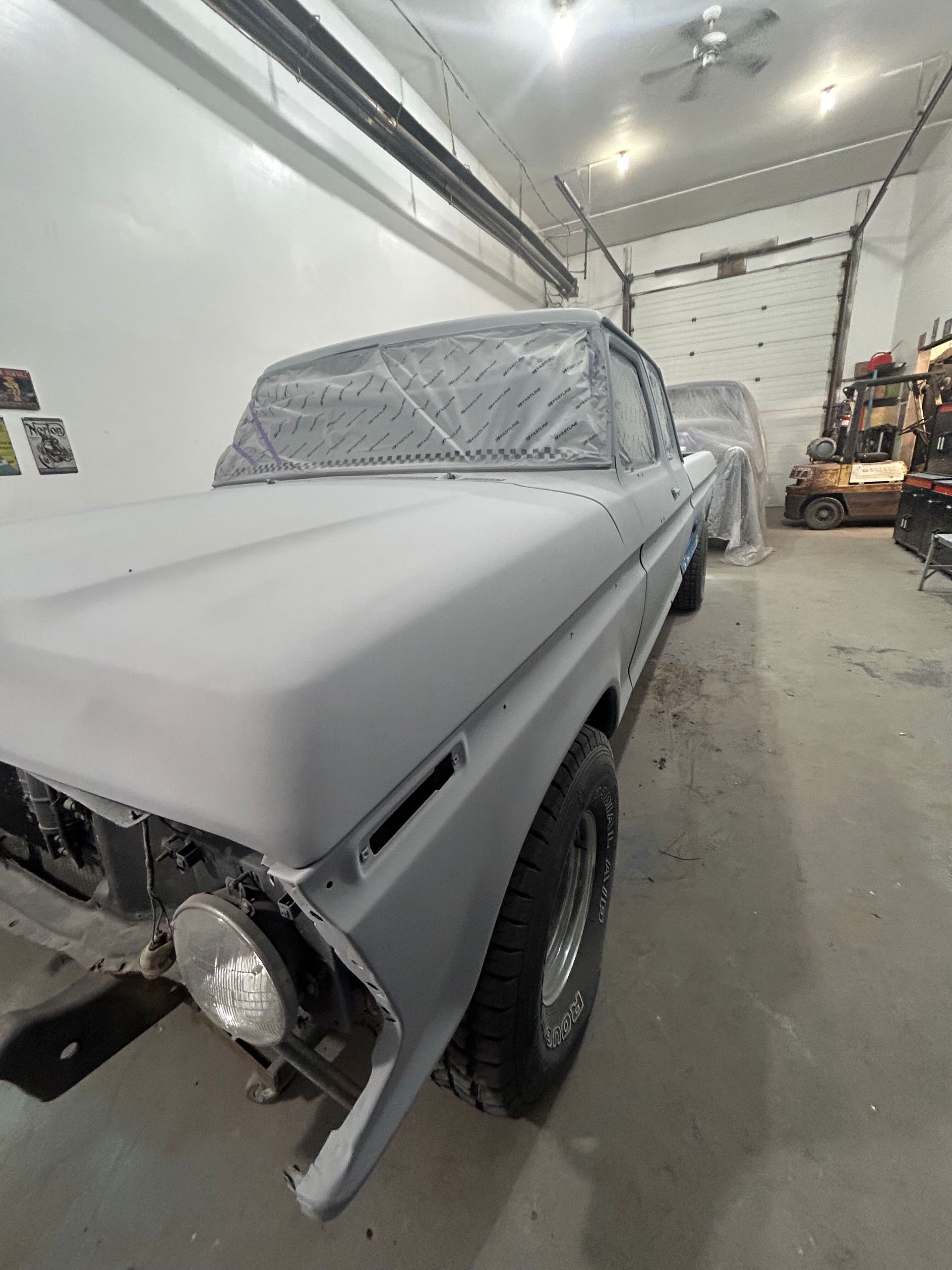 Gray classic car covered in masking paper inside an auto body shop, mid-restoration