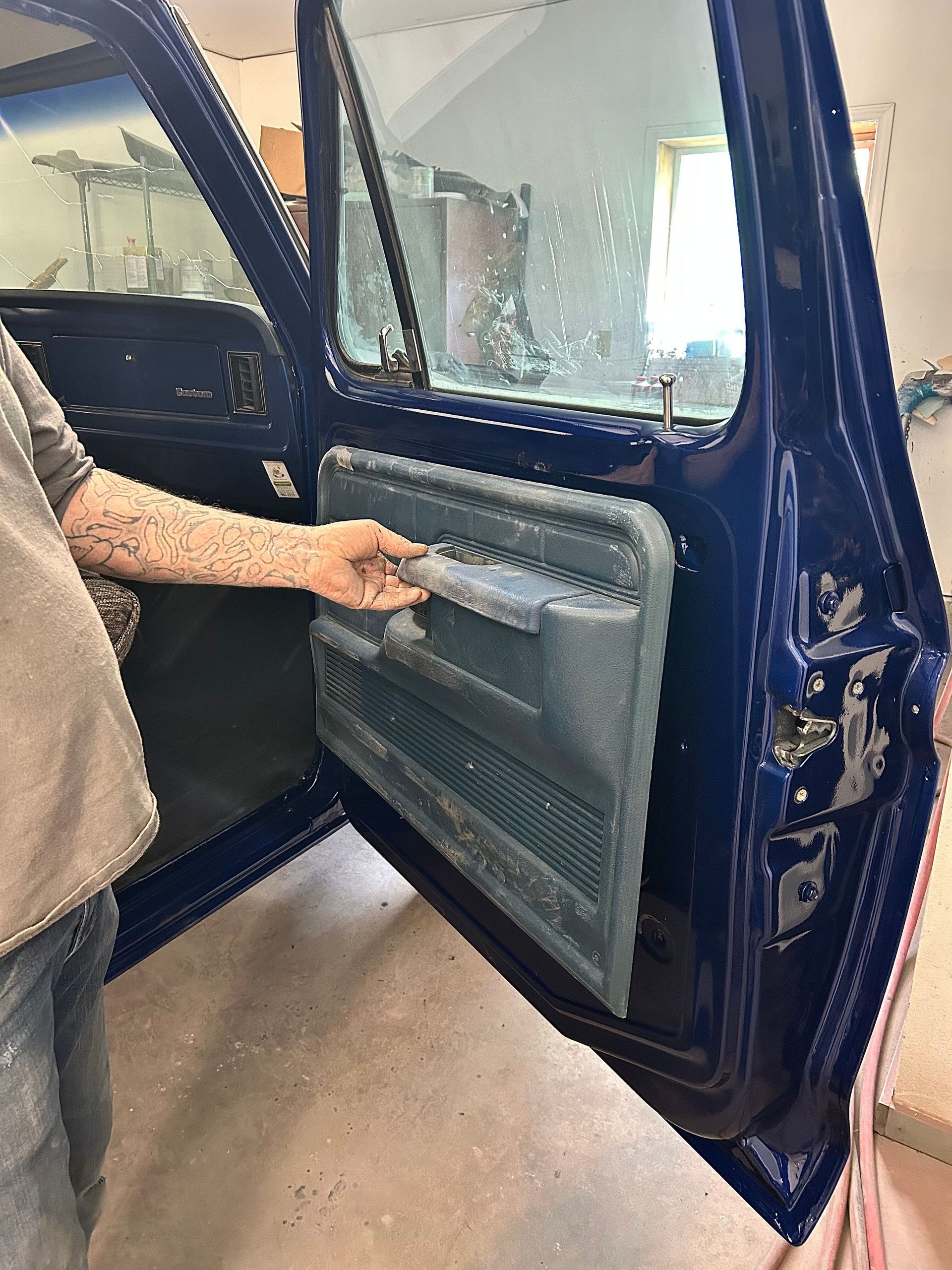 Person opening the interior door panel of a dark blue car, showing exposed wiring and insulation.