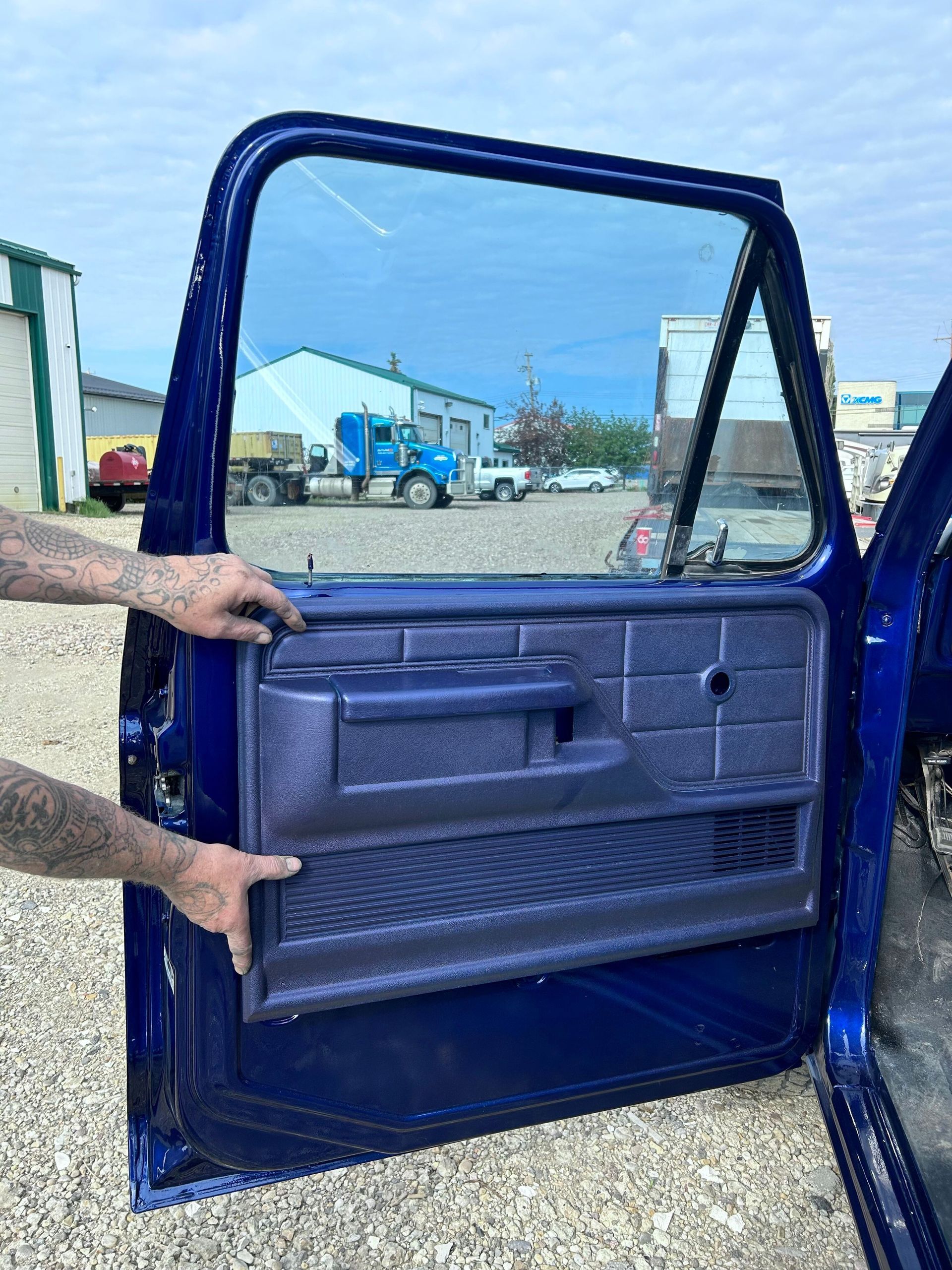 Open blue truck door with a hand holding it open in an outdoor industrial lot.