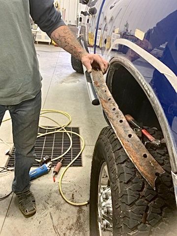 A man is working on the fender of a truck in a garage.