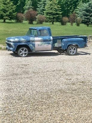 An old blue truck is parked in a gravel lot.