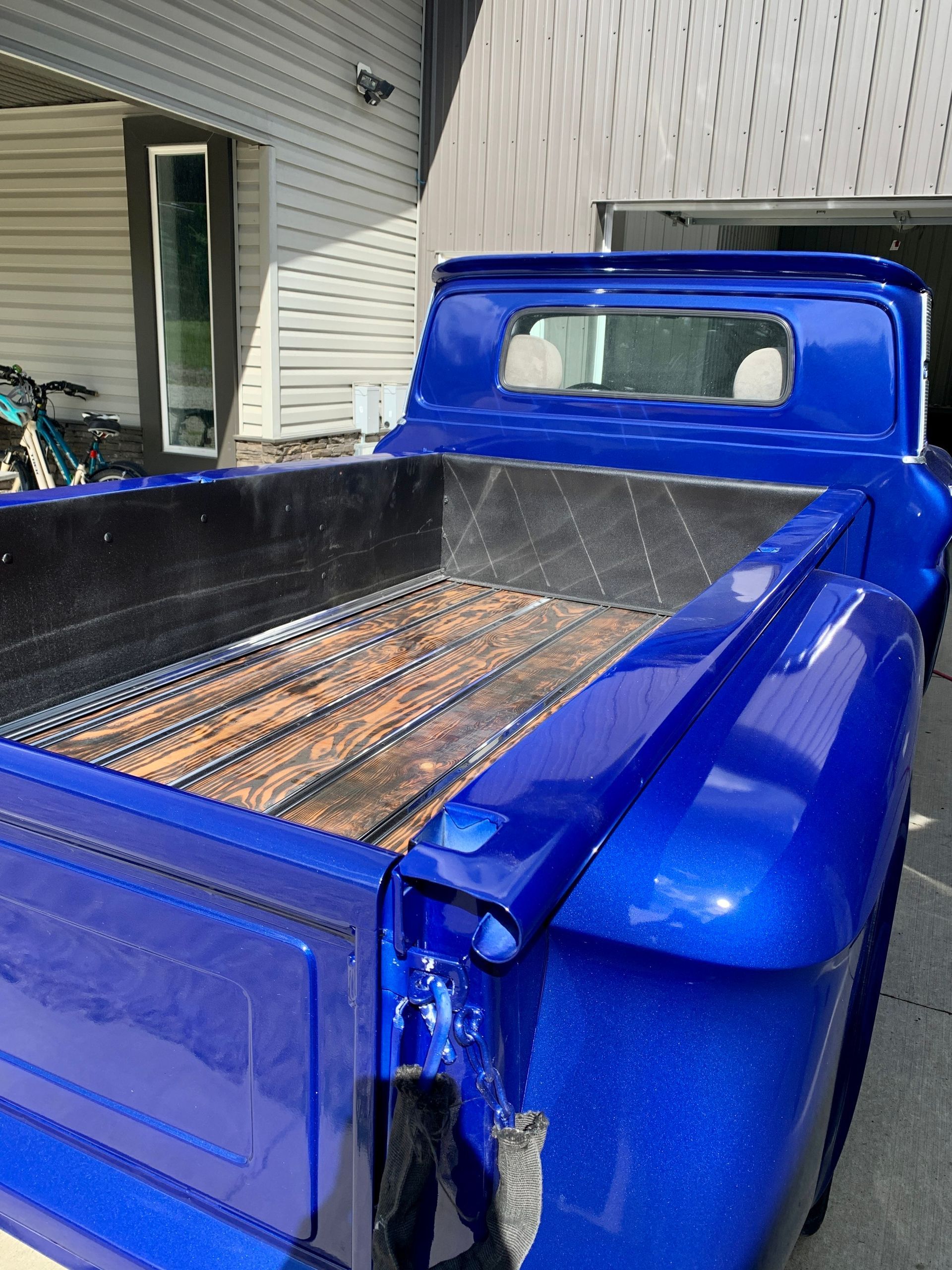 A blue truck with a wooden bed is parked in front of a house.