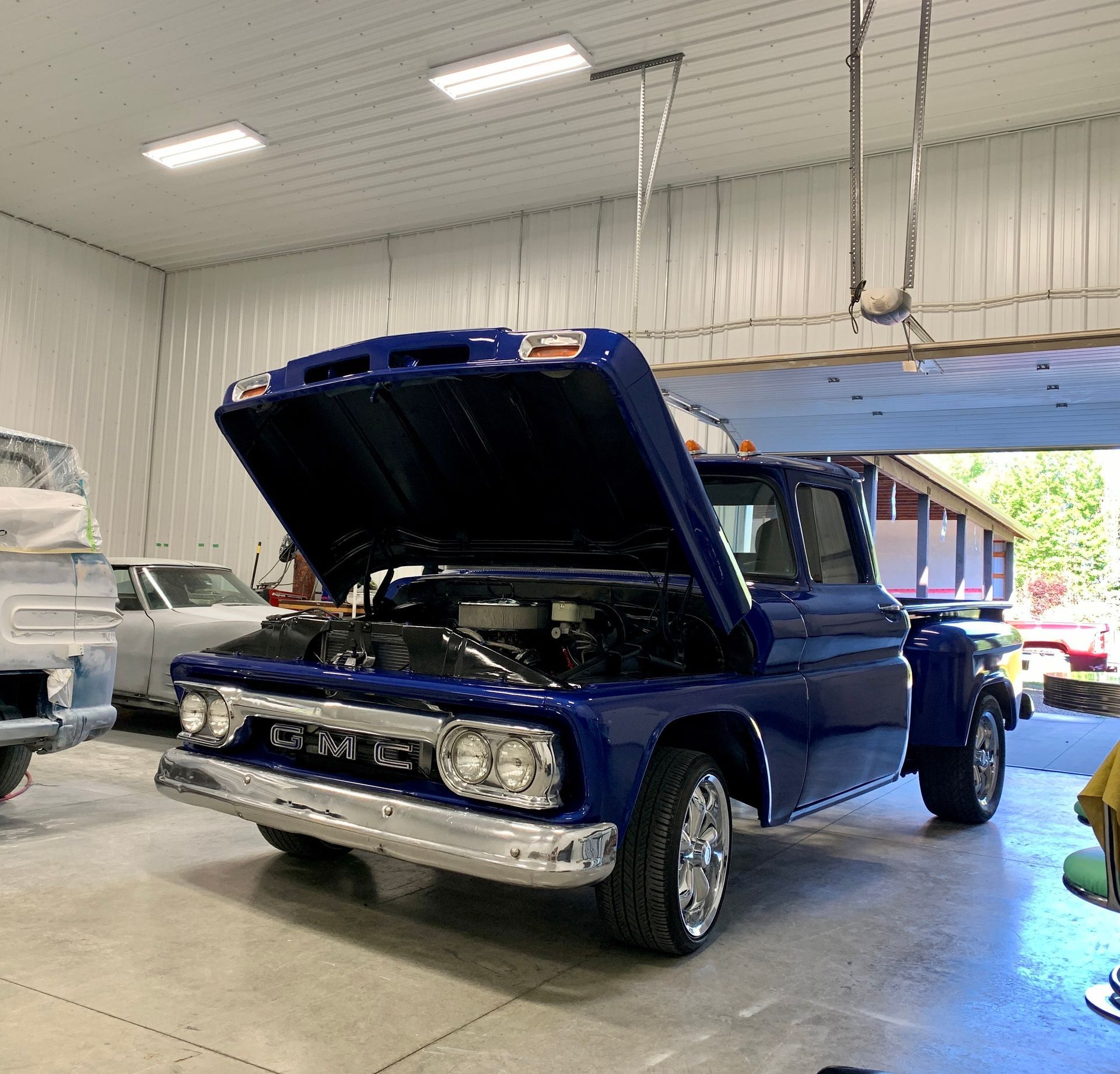 A blue gm truck is parked in a garage with its hood open.